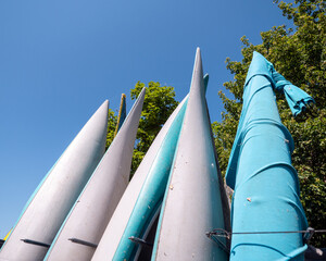 Low angle view of colorful kayaks stored upright on an outdoor rack, ready for paddling, canoeing and water sports under a clear blue summer sky. © Marek
