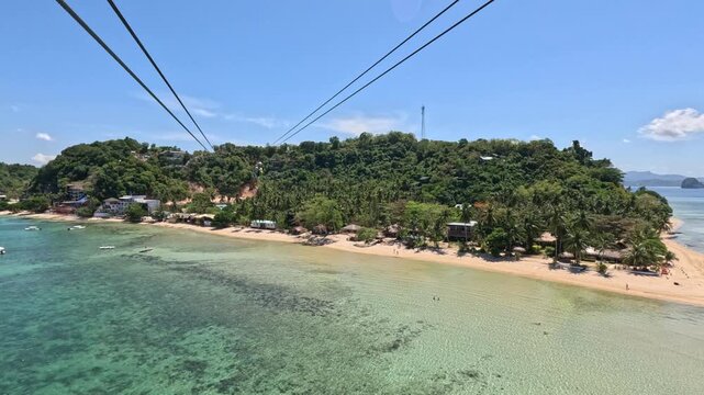 A woman secured with harnesses rides a long zipline over a beautiful Philippine island, with a beach, houses, and turquoise sea visible below on a bright sunny day.