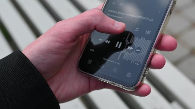 Human thumb pressing the pause button on a phone music player interface