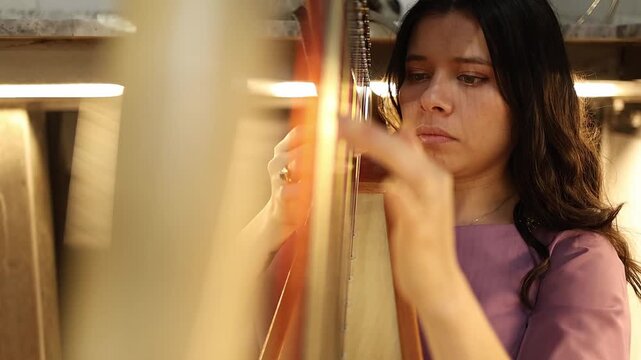Cinematic close-up shot of a woman playing a harp indoors, fingers skillfully plucking strings. Soft, golden lighting creates an artistic, focused, and intimate atmosphere.