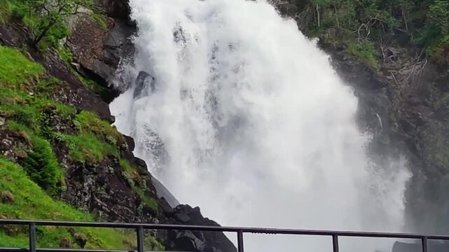 This waterfall splits into twin cascades, where the Lateelva River rushes beside a mountain road through rugged cliffs. Latefossen, Odda, Norway.