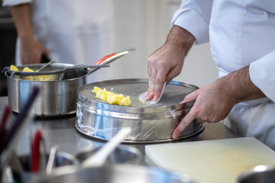 Professional Chef Hand Pressed Mashing Boiled Potatoes Through Drum Sieve Pot with Plastic Scraper Working in Restaurant Kitchen