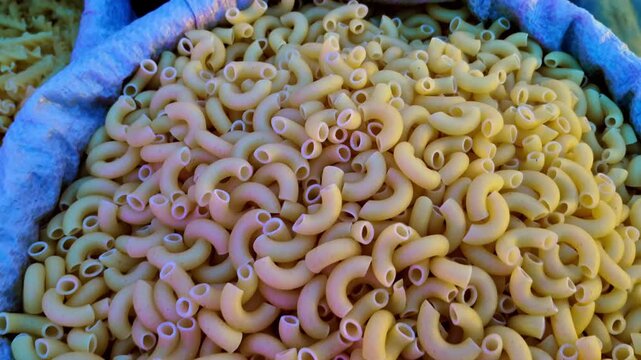 A sack of uncooked elbow macaroni pasta displays evenly shaped pieces with smooth surfaces and uniform colour. Neatly arranged pasta creates a tidy presentation within the sack.
