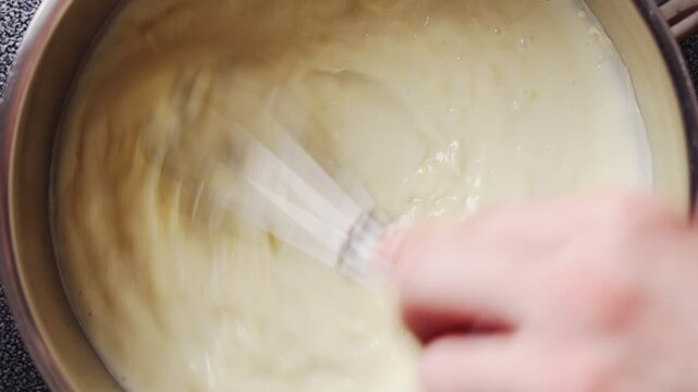 Grated parmesan goes into cheese sauce, whisk mixing in close up. Cheese sauce turns thick and creamy, perfect for Alfredo pasta. Cheese sauce works well with fettuccine, penne, spaghetti or ravioli.