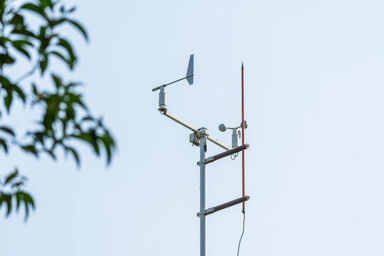 Weather monitoring instruments including anemometer and wind vane mounted on a metal pole, with a tree branch in the background.