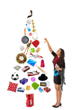 Young woman decorating a Christmas tree made with presents. 