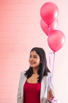 Young woman standing with helium balloons in hand.