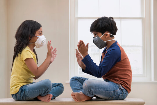 Siblings playing inside their home wearing masks due to terrible air pollution outside. (Children)  