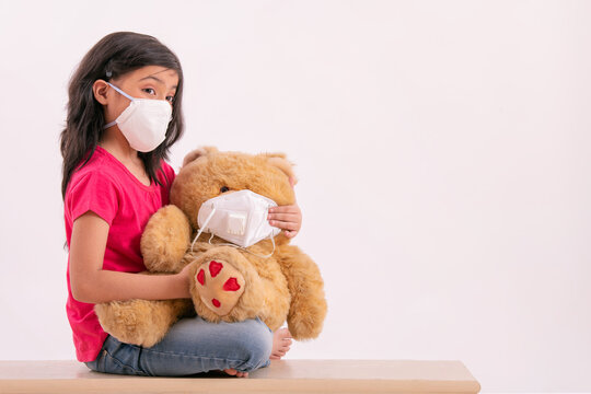 Young girl putting a pollution mask on her teddy bear as her due to terrible weather outside. (Children) 