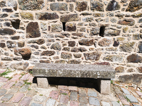 A rustic stone bench rests against an old masonry wall along a paved street. Perfect for travel guides, architectural articles, and heritage brochures.