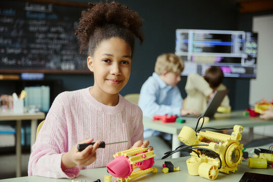 Portrait of Black girl assembling robotics project in classroom, learning engineering and coding skills. Ideal for STEM education, youth innovation, technology learning campaigns