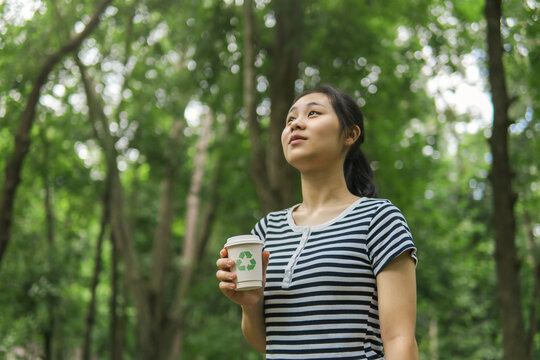 The concept of sustainable environmental practices, recycling plastic to achieve zero waste, ecology, and environmental conservation. woman holding a paper cup with a recycling symbol.