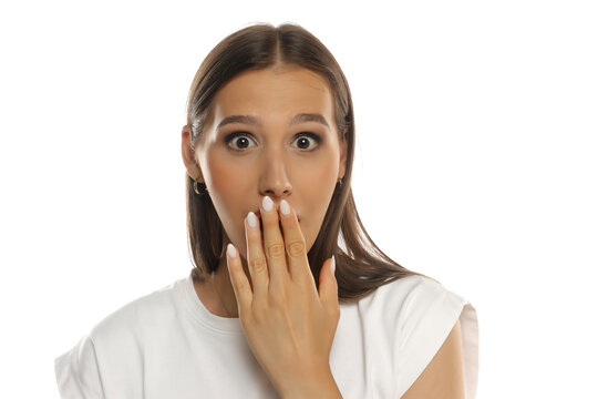 Portrait of a shocked woman covering mouth with hand, wide eyes, makeup, on white background.