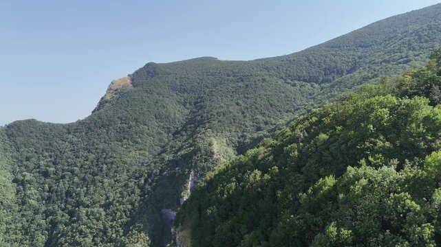 Montagne ricoperte da vegetazione verde con pendii ripidi, foresta densa e affioramenti rocciosi, sotto un cielo limpido