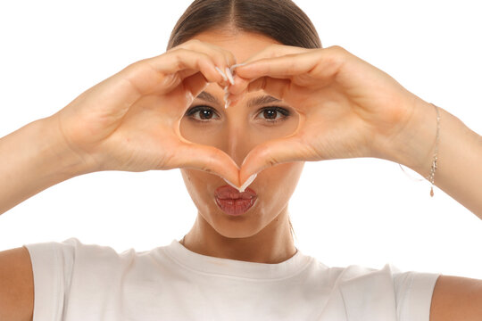 Portrait of woman making heart hand gesture around eyes, kissing lips, love concept, on white background.