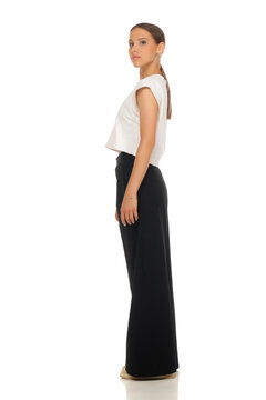 Full length side profile fashion portrait of woman, white crop top and black trousers, studio shot.