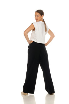 Full length rear view fashion portrait of woman looking back over shoulder, hands on hips, on white background
