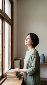 Serene woman gazing through window with old books in minimal quiet interior