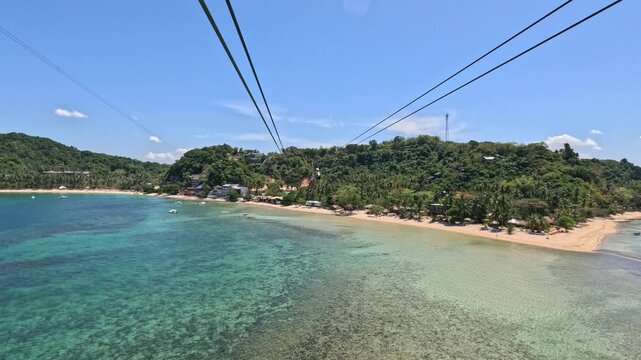 A young woman secured with harnesses rides a zipline over a tropical island beach in the Philippines on a sunny day, with ocean, mountains, and coastline views.