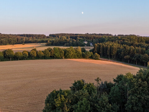 Aerial View of Harvested Farmland and Forest at Golden Hour with Moon Rising Over the Peaceful Countryside