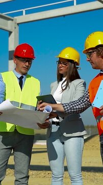 Construction Managers and Female Architect Discussing Blueprint on Site. This vertical video visualizes the concept of modern industrial development, corporate teamwork, and diverse leadership.