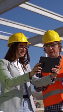 Diverse Construction Team with Blueprint and Digital Tablet Reviewing Project on Future Factory Construction Site - Vertical Slow Motion. Teamwork  and high-end infrastructure development concept.