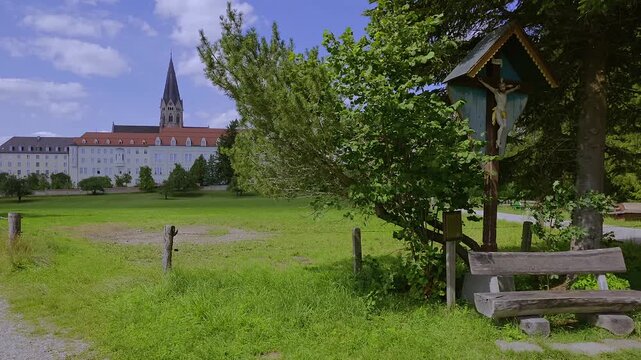 Wegkreuz und Bank dahinter die Erzabtei Sankt Ottilien, Kloster der Missionsbenediktiner, Eresing, Bayern, Deuschland