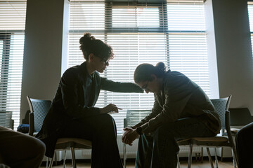 Naklejka na ściany i meble Wide shot of young adult female therapsit and patient sitting in support group therapy session, comforting during emotional discussion. Ideal for mental health, counseling, recovery marketing