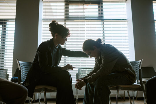 Wide shot of young adult female therapsit and patient sitting in support group therapy session, comforting during emotional discussion. Ideal for mental health, counseling, recovery marketing