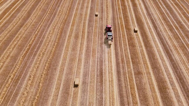 Aerial view of red square baler machinery baling straw on farmland after harvest