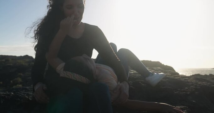 Happy young mother having playful time with female child on the beach during sunset time - Mom day, childhood and family lifestyle concept - UGC content