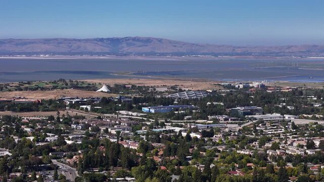 Aerial panoramic view of Google headquarters campus in Mountain View California with San Francisco Bay salt ponds marshlands and East Bay hills in the background on a clear day