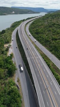 Vertical video Aerial view of highway running along river and green hills. Transportation, infrastructure, travel and logistics concept