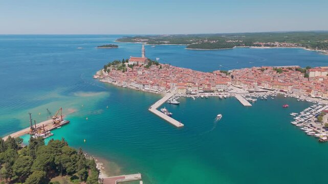 A backward drone flight over Rovinj showing the old‑town peninsula and Katarina Island emerging behind it, set against the Adriatic Sea.