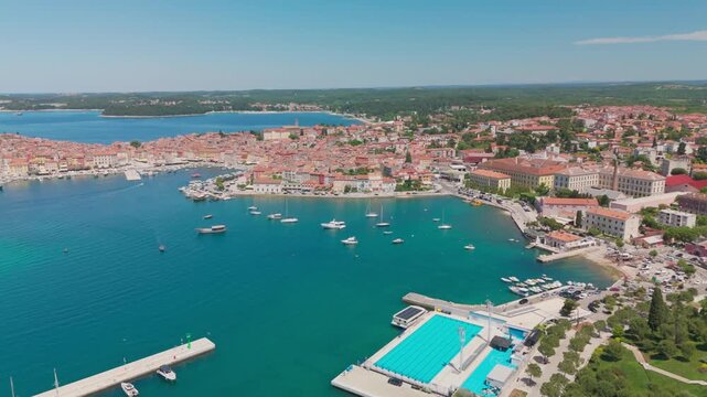 Drone turning in place over Rovinj, revealing a wide panorama of the old town and Adriatic, with a boat gliding across the water and leaving a white foam trail.