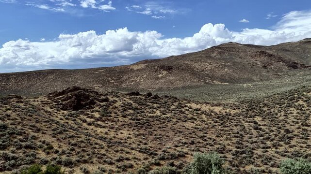 Sweeping aerial footage soars above green pastureland framed by dramatic volcanic hills near Picabo, Idaho, under bright daylight and dynamic clouds, capturing this unspoiled western landscape.