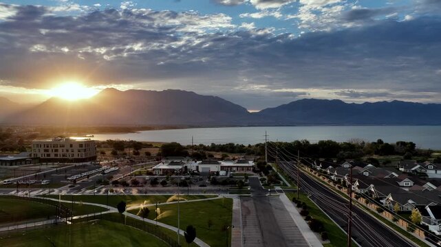 Aerial flyover at sunrise shows transmission towers and high-capacity power lines delivering energy to a new Saratoga Springs suburb by Utah Lake beneath the Wasatch Front