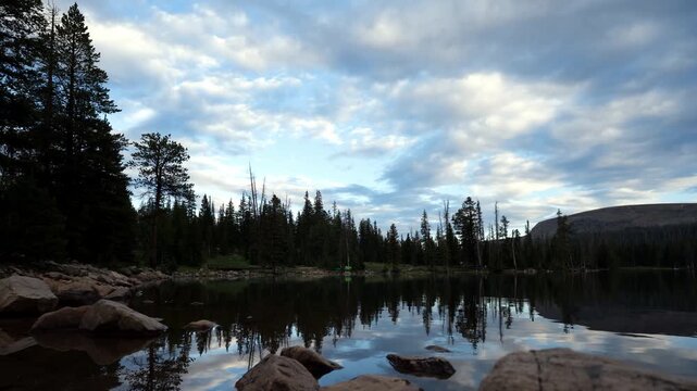 Stunning time lapse transitions from vibrant sunset to star-filled night as the Milky Way core crosses the sky above Mirror Lake, reflecting pine forests and rugged peaks in the Uinta Mountains.