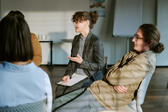 Young adult therapist leading support group discussion with adults, facilitating mental health counseling and peer sharing. Ideal for therapy, recovery, wellness marketing