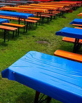 Tables are set in a park for an outdoor event or gathering with blue and orange table covers on a grassy area