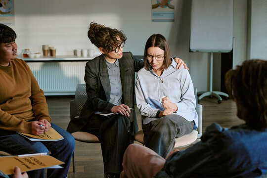 Diverse young adults attending support group therapy session, counselor comforting distressed young Caucasian woman while participants listening. Ideal for mental health care campaigns