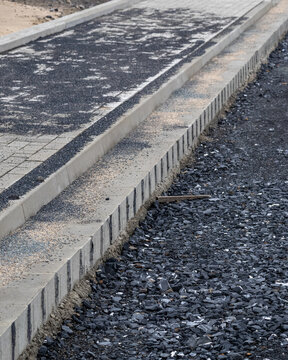 Construction work on a new walkway near a beach area with fresh asphalt and stone laid in an organized manner