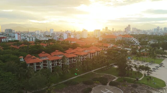 Da nang city skyline featuring resort hotels with red tile roofs and lush palm trees, basking in the glow of a warm tropical sunset, creating an inviting travel and tourism destination view