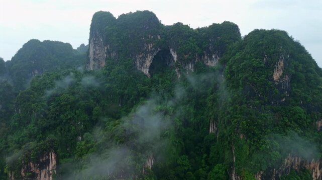 Aerial view of majestic limestone mountains surrounded by lush green tropical forest and morning mist in Krabi, Thailand.