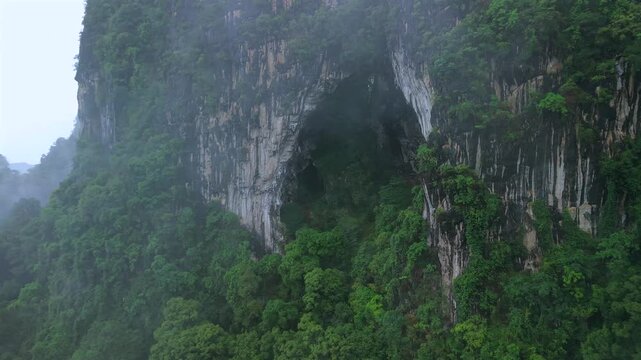 Aerial view of majestic limestone mountains surrounded by lush green tropical forest and morning mist in Krabi, Thailand.