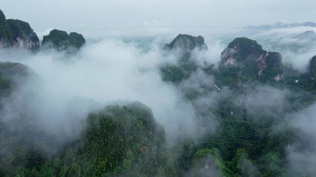 Aerial view of majestic limestone mountains surrounded by lush green tropical forest and morning mist in Krabi, Thailand.