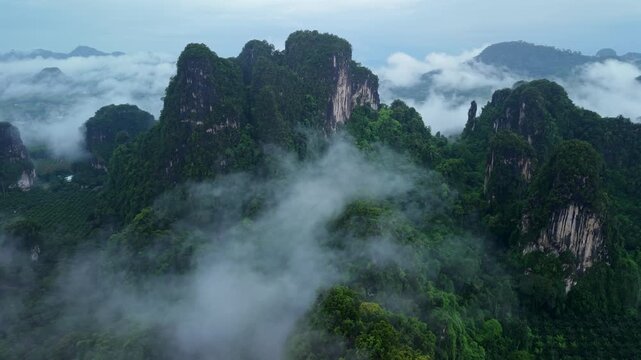 Aerial view of majestic limestone mountains surrounded by lush green tropical forest and morning mist in Krabi, Thailand.