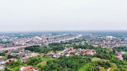 Fototapeta premium Aerial view of a sprawling town with lush green trees and a long road.