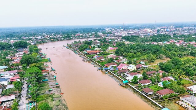 Aerial view of a brown river flowing through a residential area in a tropical village.