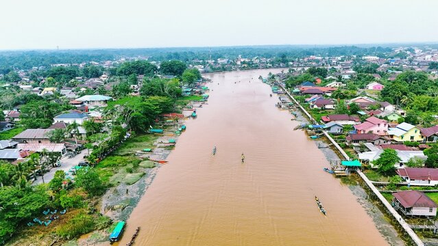Aerial view of a brown river flowing through a residential village in rural Indonesia.